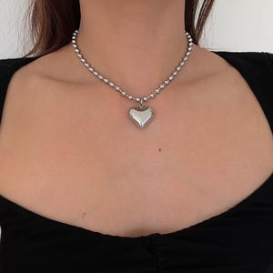 May include: A silver chain necklace with a large, silver heart pendant.