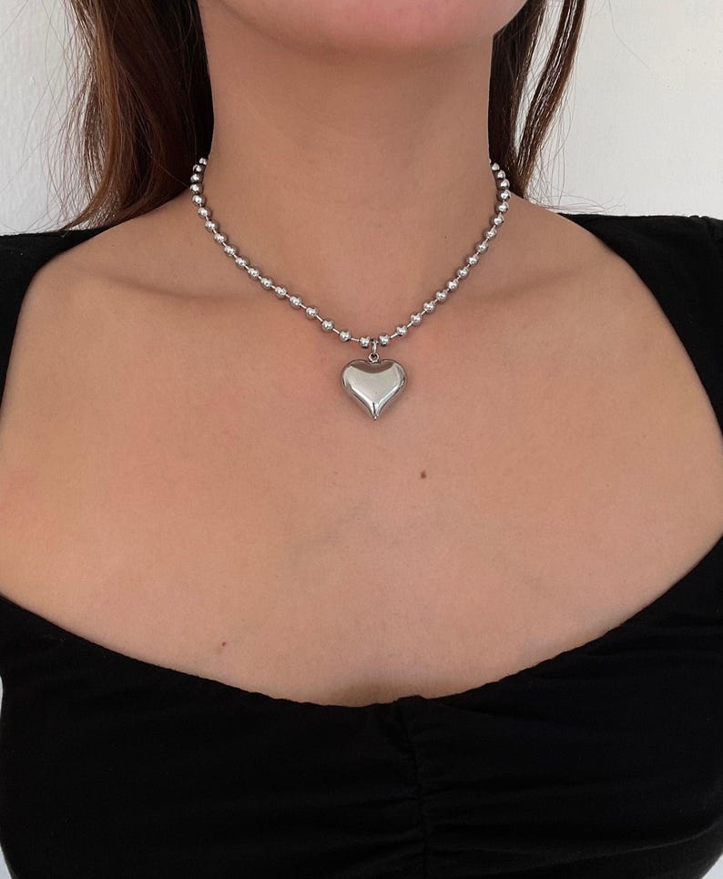 May include: A silver chain necklace with a large, silver heart pendant.