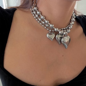 May include: A silver choker necklace with three strands of linked beads and three heart-shaped charms.