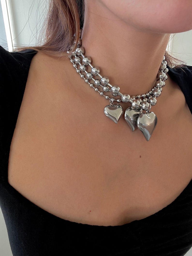 May include: A silver choker necklace with three strands of linked beads and three heart-shaped charms.