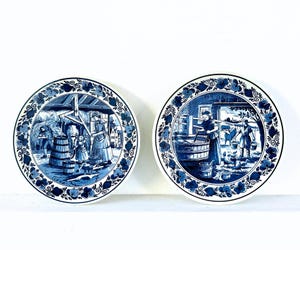 May include: Two blue and white Delftware decorative plates featuring scenes of Dutch life. One plate depicts a woman and child at a well, while the other shows a woman washing clothes.