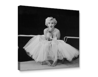May include: Monochrome canvas print featuring a woman in a white tulle skirt and strapless top, seated. The image is a portrait, with the woman's hands near her face. A ballet barre is visible in the background.