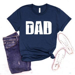 May include: A navy blue t-shirt with the word "DAD" in white letters. The letters are decorated with a hammer, wrench, and screwdriver.