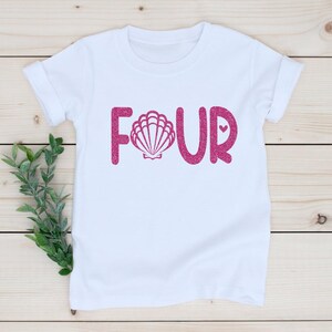 May include: White t-shirt with pink glitter lettering that says "FOUR" with a pink glitter seashell in the "O".