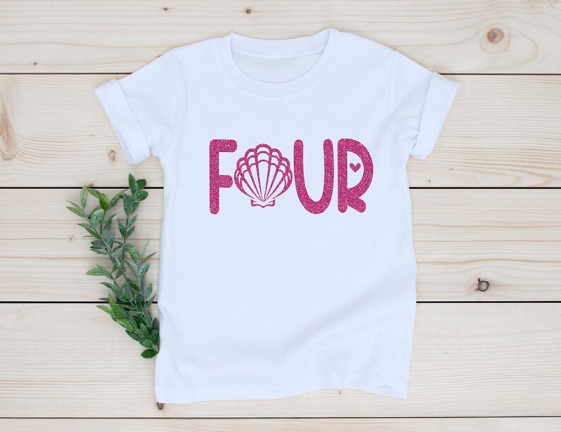 May include: White t-shirt with pink glitter lettering that says "FOUR" with a pink glitter seashell in the "O".