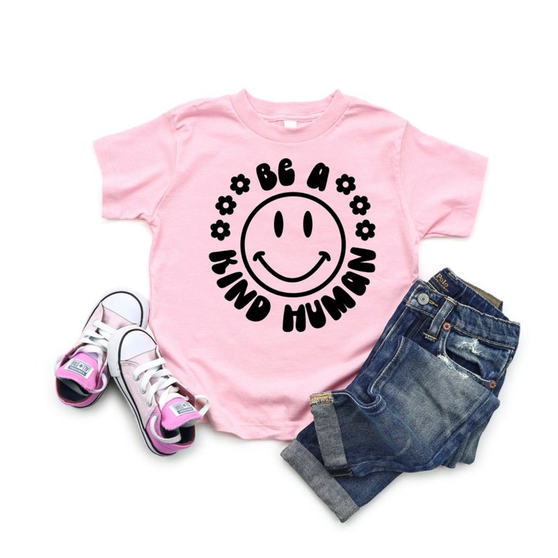 May include: Pink t-shirt with a black smiley face and the text "Be a Kind Human" in a circle around the smiley face.