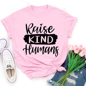 May include: Pink t-shirt with black text that reads "Raise Kind Humans".