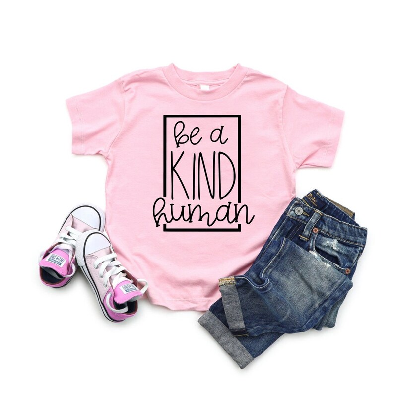 May include: Pink t-shirt with black text that reads "be a kind human" inside a black box.