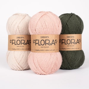 May include: Three balls of yarn in beige, pink, and green. Each ball has a brown paper label that reads "DROPS FLORA UNI COLOUR Everyday comfort in alpaca and wool."