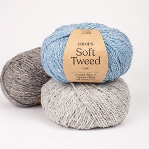 May include: Three balls of yarn in different colours: light blue, grey, and a darker grey. The light blue ball has a label that reads "DROPS Soft Tweed mix. A tweed classic in Superfine Alpaca and Merino Wool."
