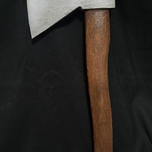 May include: A silver axe with a brown wooden handle. The axe head has a slight curve to it.