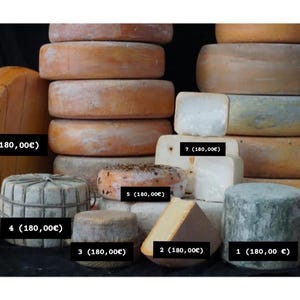 Op de afbeelding: Assortiment van ronde kazen, sommige gestapeld, andere individueel gepresenteerd. De kazen zijn in verschillende kleuren, waaronder wit, geel, bruin en groen. De kazen zijn gelabeld met nummers en prijzen in euro.
