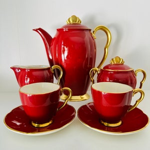 May include: A red and gold tea set comprising a teapot, creamer, sugar bowl, and two cups and saucers. The set is vintage in style and made of fine china.