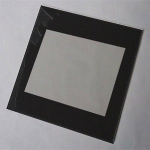May include: A black picture frame with a white mat. The frame is rectangular with a black border and a white interior mat. The frame is angled slightly, showing the corner and the protective plastic covering.
