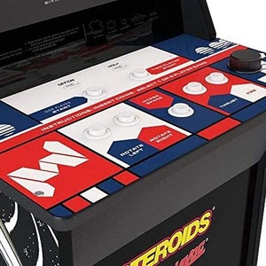 May include: Close-up of an arcade game control panel. The panel features a red, white, and blue color scheme with various buttons and a joystick. Text on the panel includes game instructions and button labels like "FIRE" and "HYPER SPACE". The game is labeled "Asteroids Deluxe".