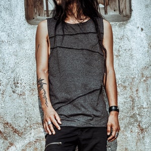 May include: A person with long black hair wearing a grey sleeveless shirt and black trousers. They have a tattoo on their arm and are wearing a bracelet on their wrist.