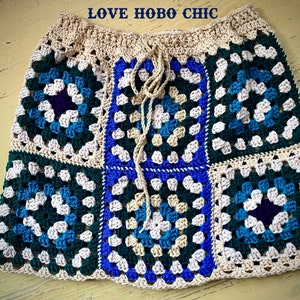 Puede incluir: Una falda de ganchillo hecha de cuadrados de la abuela en tonos de azul, verde, blanco y beige. La falda tiene una cintura con cordón y está atada con un cordón beige.