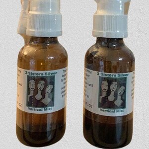 May include: Two brown glass bottles with silver spray tops and labels that say "3 Sisters Silver Vertical Mist". The labels feature a green illustration of three women with long hair.