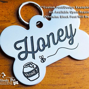 K&ouml;nnte beinhalten: Silberner, knochenf&ouml;rmiger Hundemarkenanh&auml;nger mit dem Namen "Honey", der in einer kursivschriftlichen Schriftart graviert ist. Eine kleine Biene und ein Honigtopf mit dem Wort "Honey" sind ebenfalls auf dem Anh&auml;nger graviert.