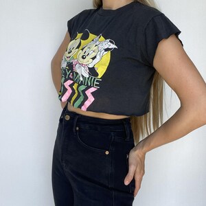 May include: Black crop top featuring Mickey and Minnie Mouse graphic. The graphic includes the text "Mickey & Minnie" with a yellow background and pink and green zig-zag design. The top is paired with black jeans.