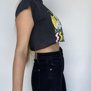 May include: Black crop top with a graphic print and dark wash jeans. The crop top has a raw hem and short sleeves. The jeans have a classic five-pocket design.