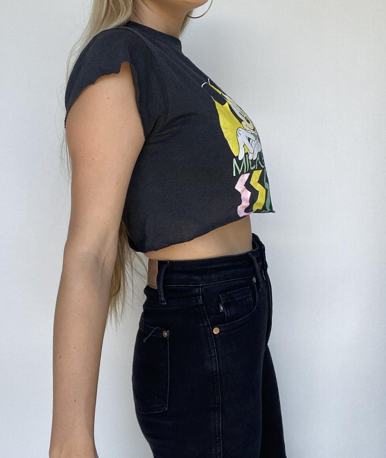 May include: Black crop top with a graphic print and dark wash jeans. The crop top has a raw hem and short sleeves. The jeans have a classic five-pocket design.
