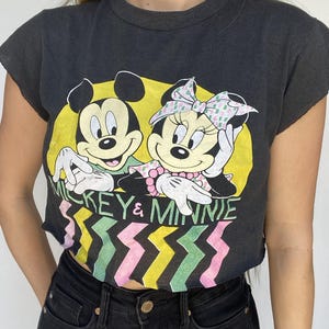 May include: Black crop top featuring Mickey and Minnie Mouse in a yellow circle. The shirt has the words "Mickey & Minnie" and a colorful zigzag pattern. The shirt is cut off at the sleeves and bottom.
