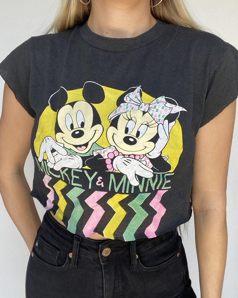 May include: Black crop top featuring Mickey and Minnie Mouse in a yellow circle. The shirt has the words "Mickey & Minnie" and a colorful zigzag pattern. The shirt is cut off at the sleeves and bottom.