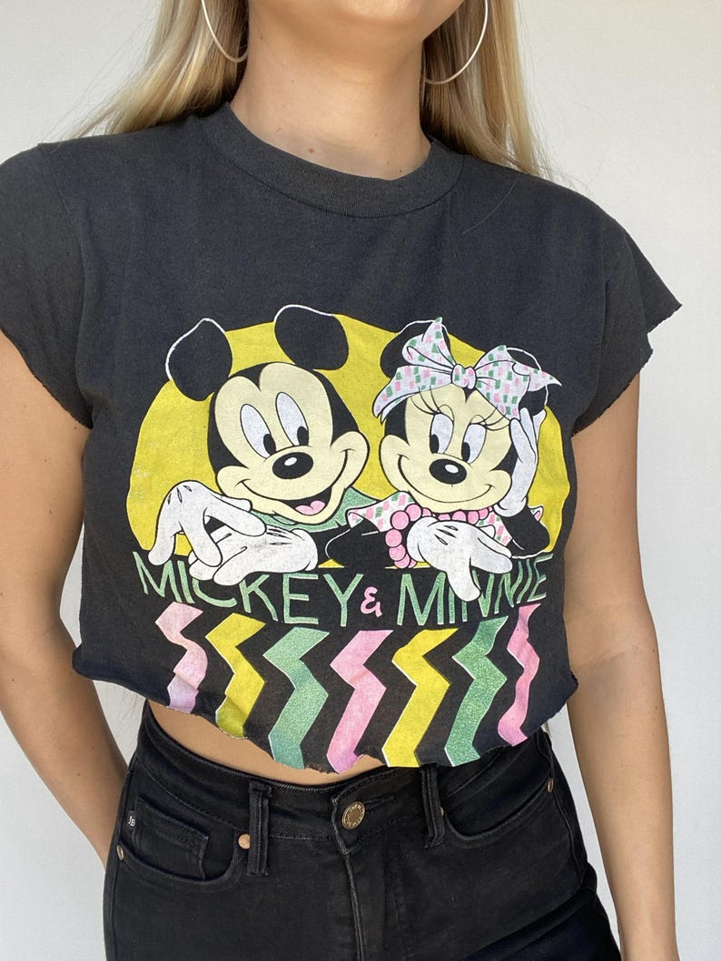 May include: Black t-shirt featuring Mickey and Minnie Mouse. The graphic shows Mickey with a yellow background and Minnie with a pink bow. The text "MICKEY & MINNIE" is above a colorful zigzag pattern.