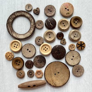 Könnte beinhalten: Eine Sammlung verschiedener Knöpfe in unterschiedlichen Größen, Formen und Brauntönen. Das Set enthält runde, herzförmige und Knebelknöpfe aus Holz und Kokosnussschale mit zwei oder vier Löchern, einige davon mit eingravierten Blumenmustern.