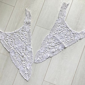 May include: Two white crocheted lace pieces, each shaped like a triangle with a rounded top. The lace has a delicate floral pattern.