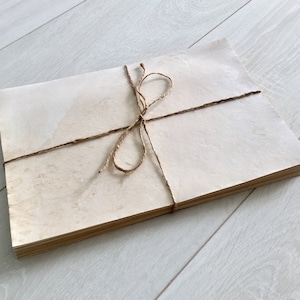 May include: A stack of blank, off-white paper sheets tied together with twine. The paper has a slightly textured surface and appears to be aged or vintage.