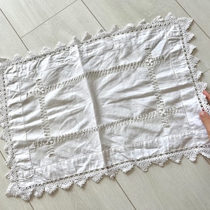 Könnte beinhalten: Weißes rechteckiges Deckchen mit gehäkeltem Spitzenrand. Die Mitte weist ein geometrisches Design mit Ausschnittdetails auf. Das Deckchen ist aus weichem Stoff gefertigt. Ein Vintage-Artikel.