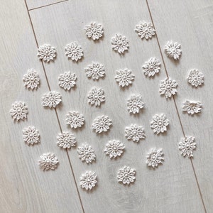 Könnte beinhalten: Eine Sammlung weißer gehäkelter Schneeflocken, die in einem Kreis auf einer hellbraunen Holzoberfläche angeordnet sind.