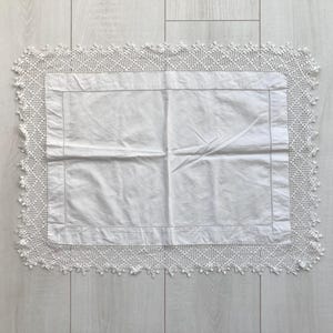 Puede incluir: Funda de almohada rectangular blanca con un borde de encaje de ganchillo. La funda de almohada está hecha de tela blanca con un borde cosido. El borde de encaje de ganchillo añade un toque delicado y hecho a mano.