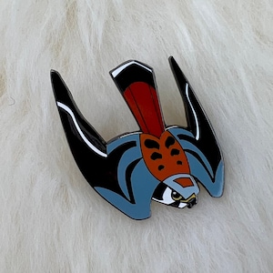 May include: A detailed enamel pin depicting a bird of prey. The pin features black wings with white detailing, a red and brown body, and a blue outline. The bird's head has a detailed eye.
