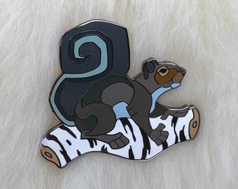 Könnte beinhalten: Eine schwarze und blaue Emaille-Anstecknadel mit einem Eichhörnchen, das auf einem weiß-schwarzen Baumstamm sitzt. Das Eichhörnchen hat einen eingerollten Schwanz und schaut nach rechts.