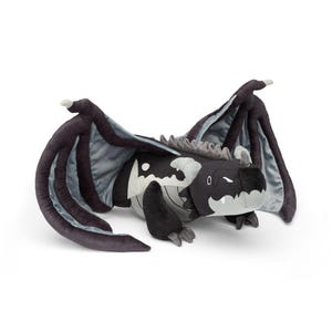 May include: A plush dragon toy in black, gray, and white. The dragon has large wings, a long body, and a smiling face. The toy is made of soft material and is designed to be cuddled.