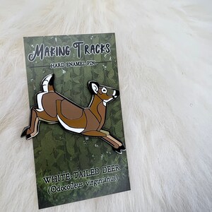 May include: White-tailed deer enamel pin with brown and white details. The pin is on a card with the text "Making Tracks" and "Hard Enamel Pin". The card also says "White-tailed Deer (Odocoileus virginianus)".