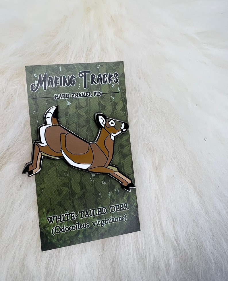 May include: White-tailed deer enamel pin with brown and white details. The pin is on a card with the text "Making Tracks" and "Hard Enamel Pin". The card also says "White-tailed Deer (Odocoileus virginianus)".
