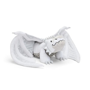 May include: A soft, white dragon toy with large wings and a friendly face. The dragon features grey accents and a polka dot pattern on the wings. A cuddly toy, designed to be soft and huggable.