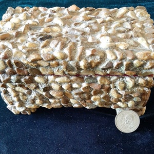May include: A small, rectangular box made of stone with a red interior. The box is made of small, rounded stones that are arranged in a random pattern. The box is closed and the top is visible.