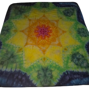 May include: A tie-dye blanket with a central starburst design. The blanket features a vibrant color palette, including yellow, orange, green, and blue hues. The starburst pattern is surrounded by a square border with a dark blue edge.
