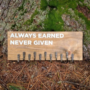 May include: Wooden key holder with the text "ALWAYS EARNED NEVER GIVEN" in white lettering. The key holder has 12 hooks.
