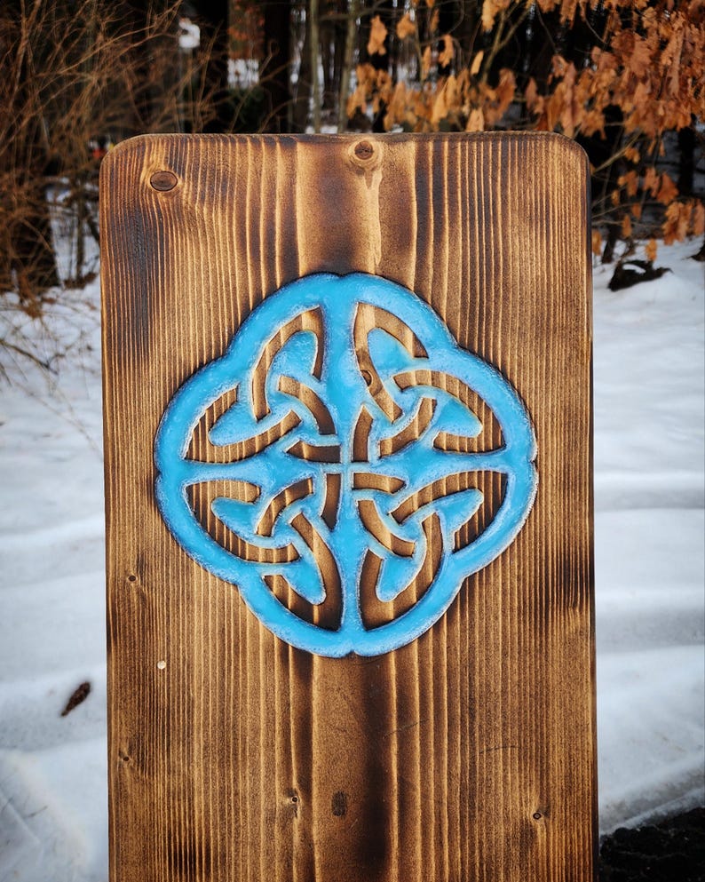 May include: A wooden sign with a blue Celtic knot design carved into the surface. The wood has a dark brown stain.