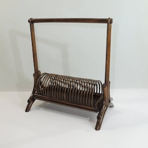 May include: A dark brown wooden magazine rack with a slatted design. The rack has a tall, rectangular frame and a curved base.