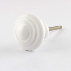 May include: A white ceramic cabinet knob with a swirl design. The knob has a round shape with a metal screw for installation. This decorative hardware is suitable for drawers, cabinets, and furniture.
