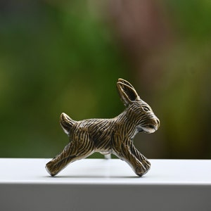 Könnte beinhalten: Eine kleine, bronzefarbene Hasenfigur, die nach vorne rennt. Die Figur ist mit Fell detailliert und hat ein realistisches Aussehen.