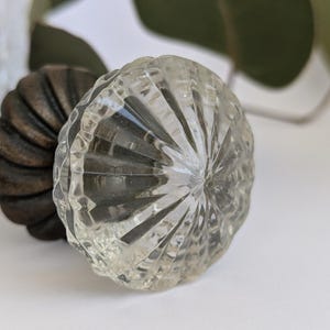 May include: A clear glass cabinet knob with a faceted design. The knob has a brown metal base.
