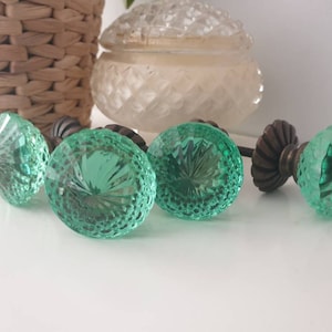 May include: Four green glass cabinet knobs with a faceted design. The knobs have a brass base and are perfect for adding a touch of vintage charm to any home.